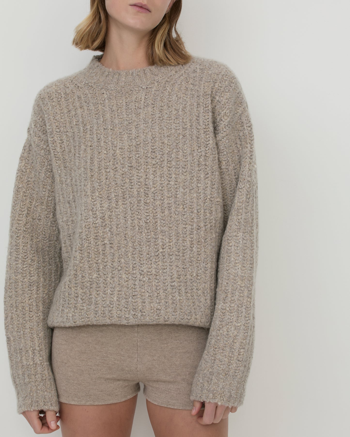 Women wearing Casasola Orso beige-colored, oversized, four-ply knitted cashmere-silk boucle sweater with a ribbed mock neckline, with knitted cashmere shorts - front view.